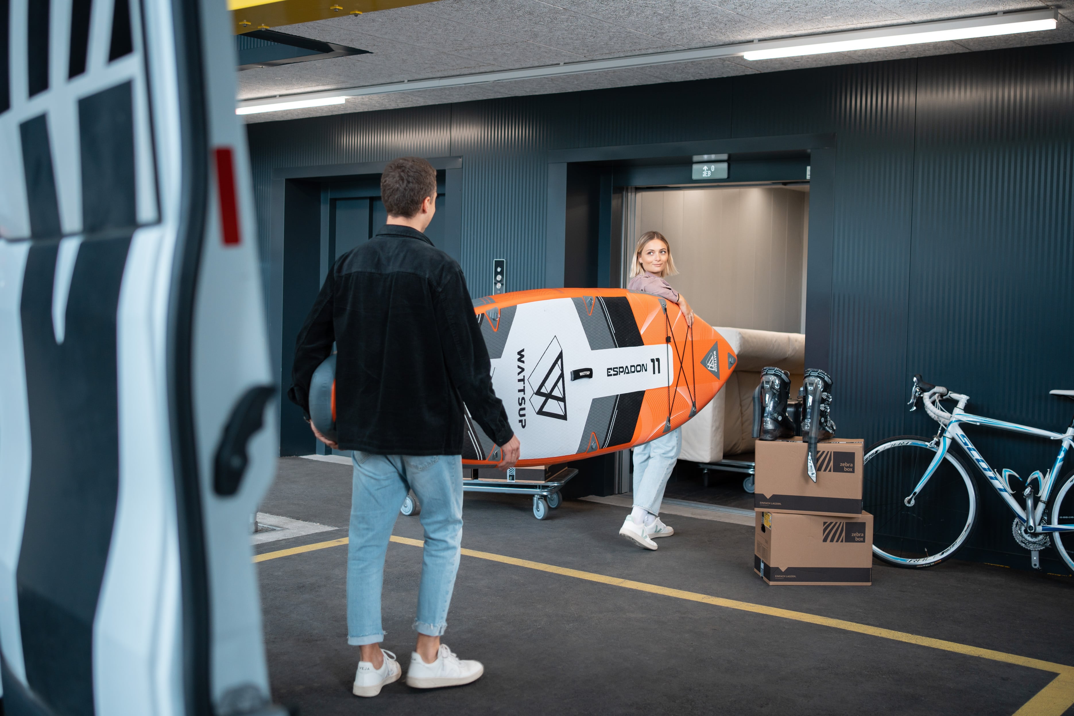 Young couple carrying a stand up paddle board into Zebrabox's goods lift.