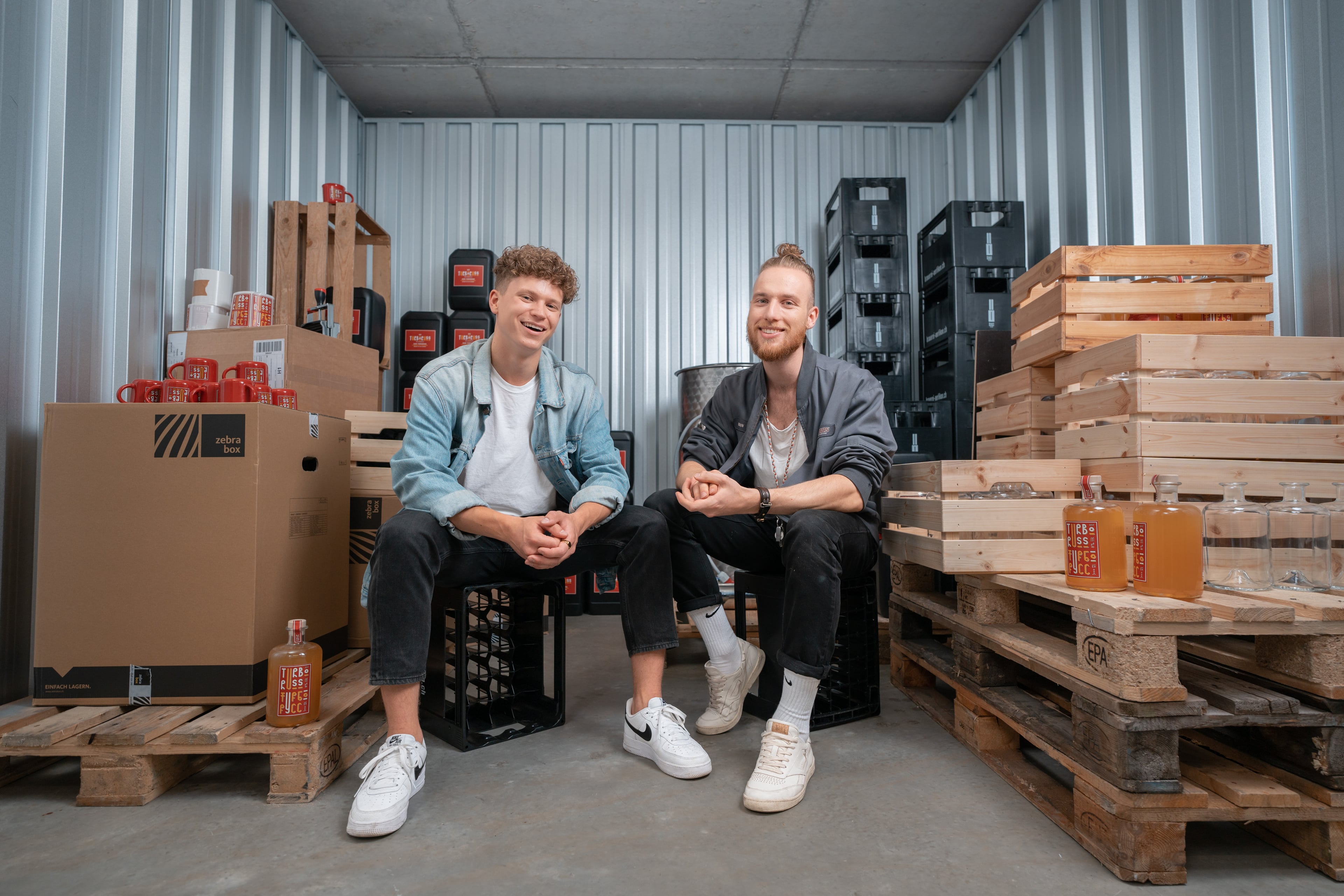 Dos jóvenes fundadores de una fábrica de cerveza se sientan en el trastero Zebrabox y miran felices a la cámara.