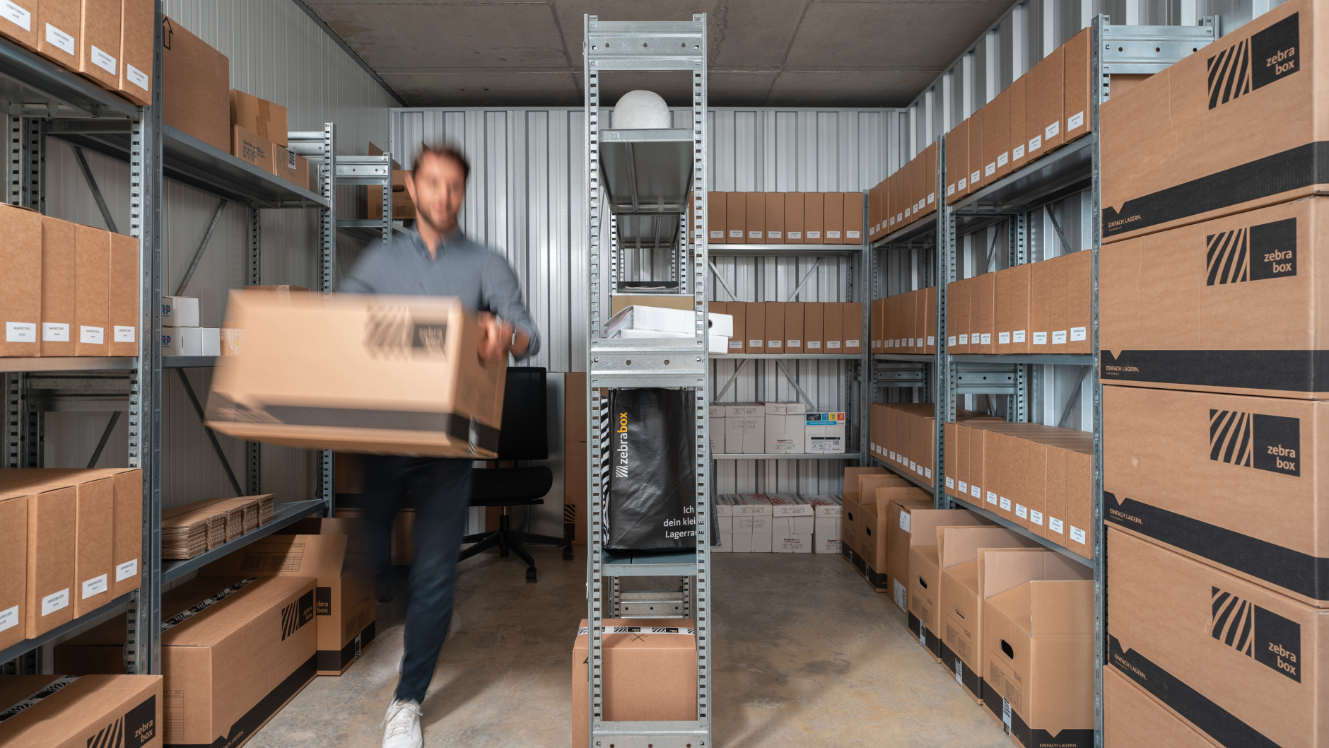 A man is walking through the Zebrabox storage unit with a moving box.