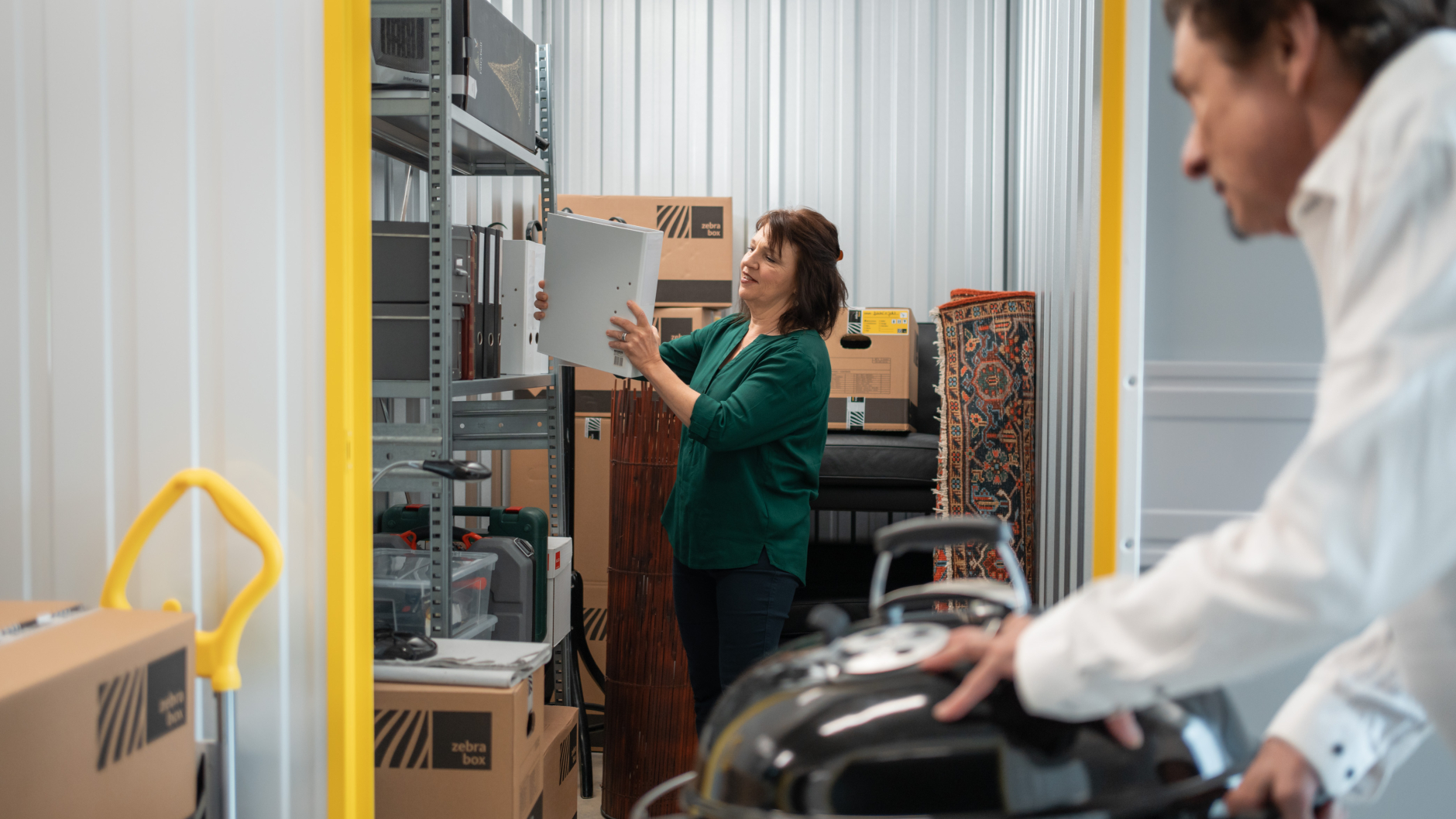 A man is rolling a kettle grill into the storage unit at Zebrabox and his wife putting folders in boltless shelves.