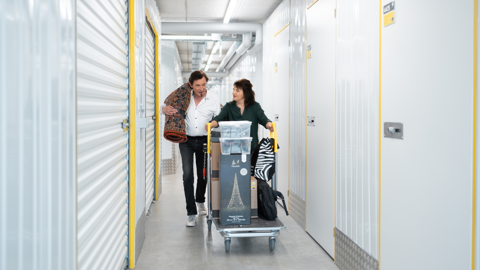 An elderly couple is walking through the Zebrabox warehouse with a filled trolley to store their household goods.