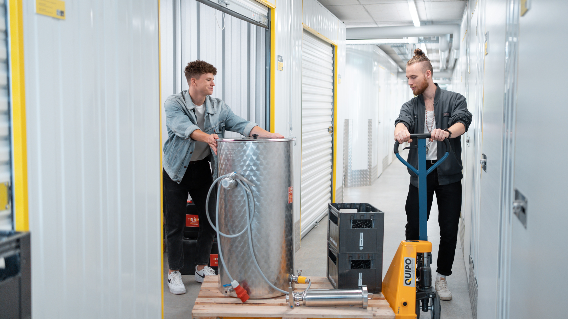 Two young start-up founders are pushing a brewing kettle on a pallet trolley into the storage unit at Zebrabox.